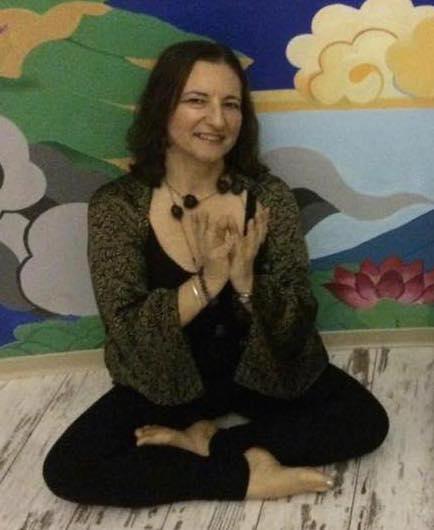 She is seated in a yoga pose with her arms crossed over her chest.