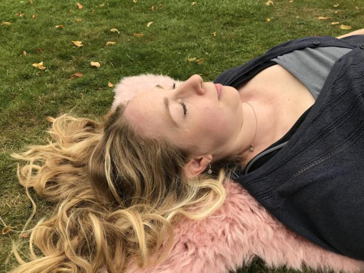 An adult girl lying on the grassy & her scattered hair feeling better after doing a Mind-body exercise