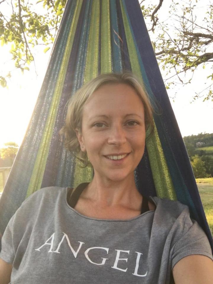 A smiley adult woman wearing a yoga brown shirt with the name "ANGEL" written in a Calibri (Body) font