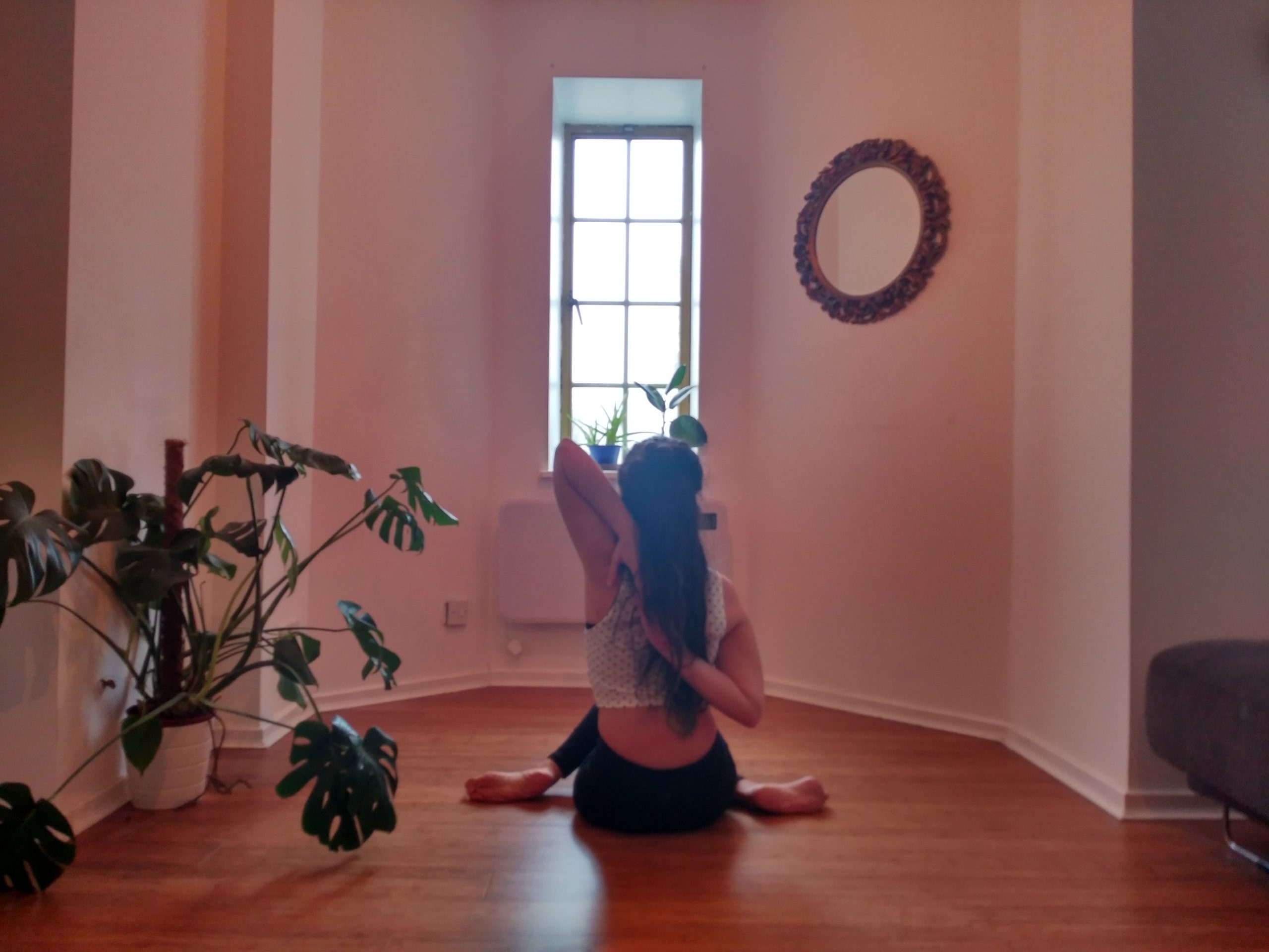 Thin-waisted woman sitting on the floor in yoga pose from the front of room's window
