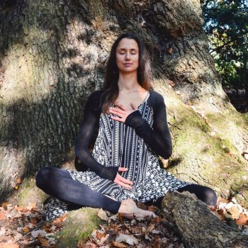 A woman is sitting in the shade of a tree in a yoga pose