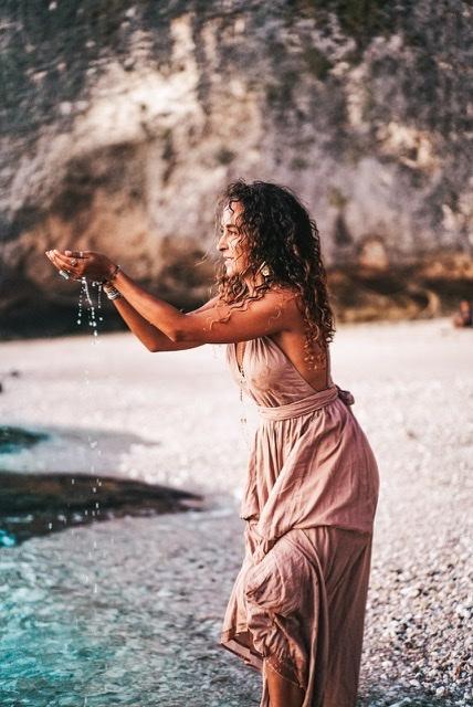 A young lady wearing sexy/yoga clothes is standing on the beach of the river and she is holding water in his hands