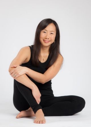 A Chinese lady sitting in Pran yoga pose on the floor and wearing black tights and a shirt