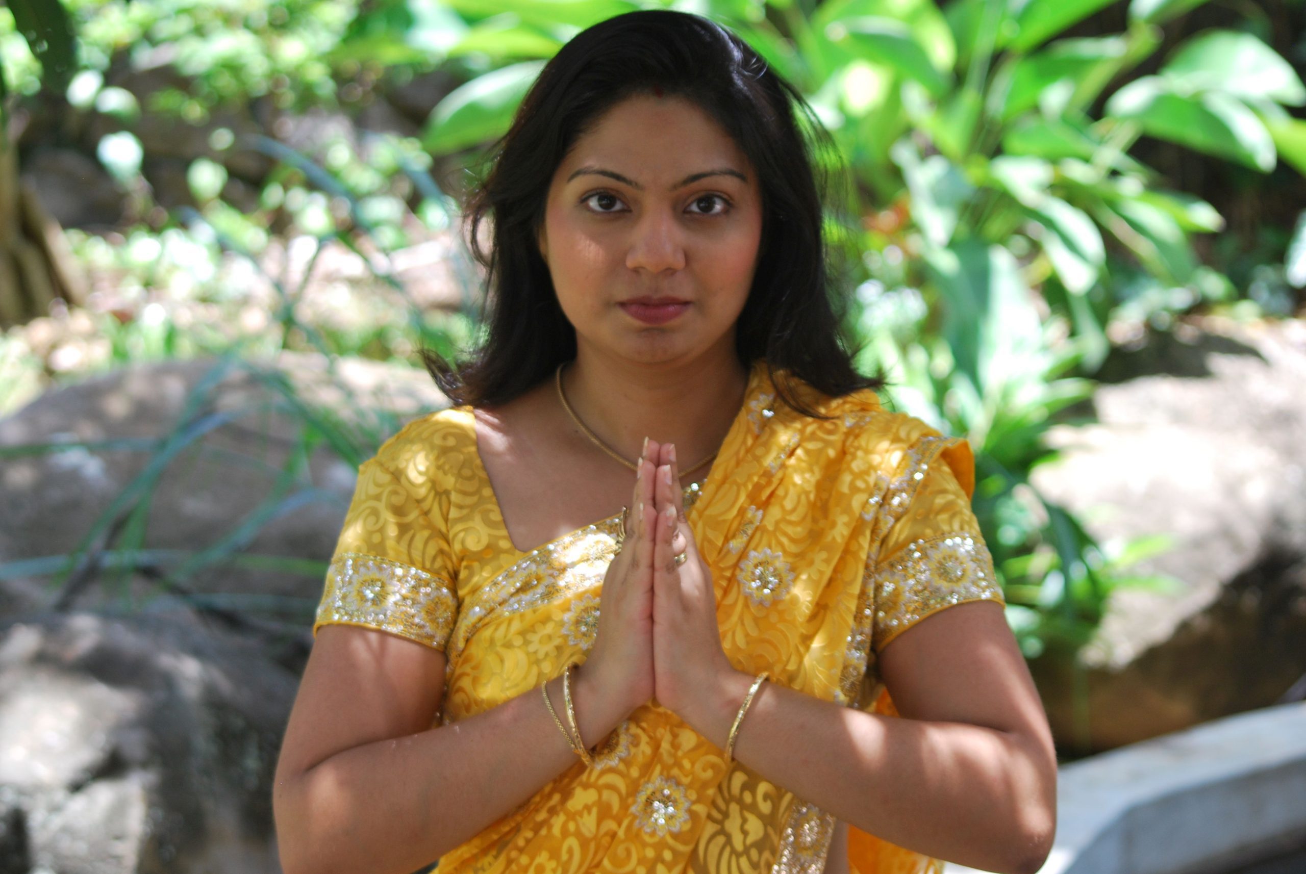 An Indian woman standing in a Womb Yoga pose, with their extended arms like a namaste