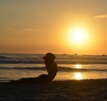 A young woman lying on the beach of see in a yoga pose with a sunset over a beautiful natural landscape