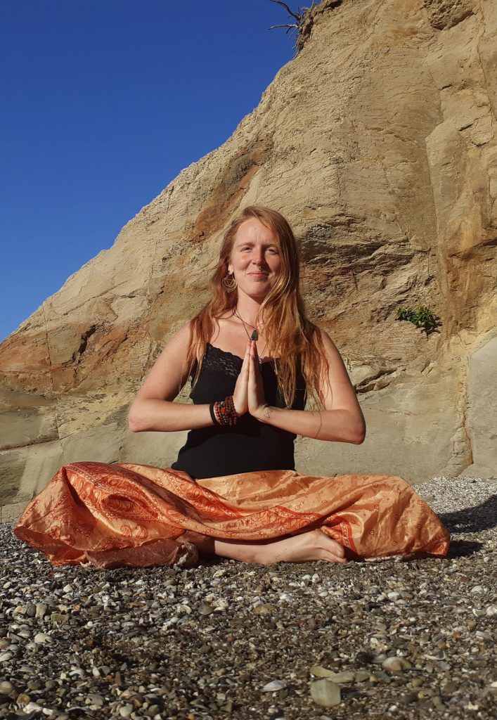 Such a beautiful young girl sitting with the Namaskar yoga pose on the rock